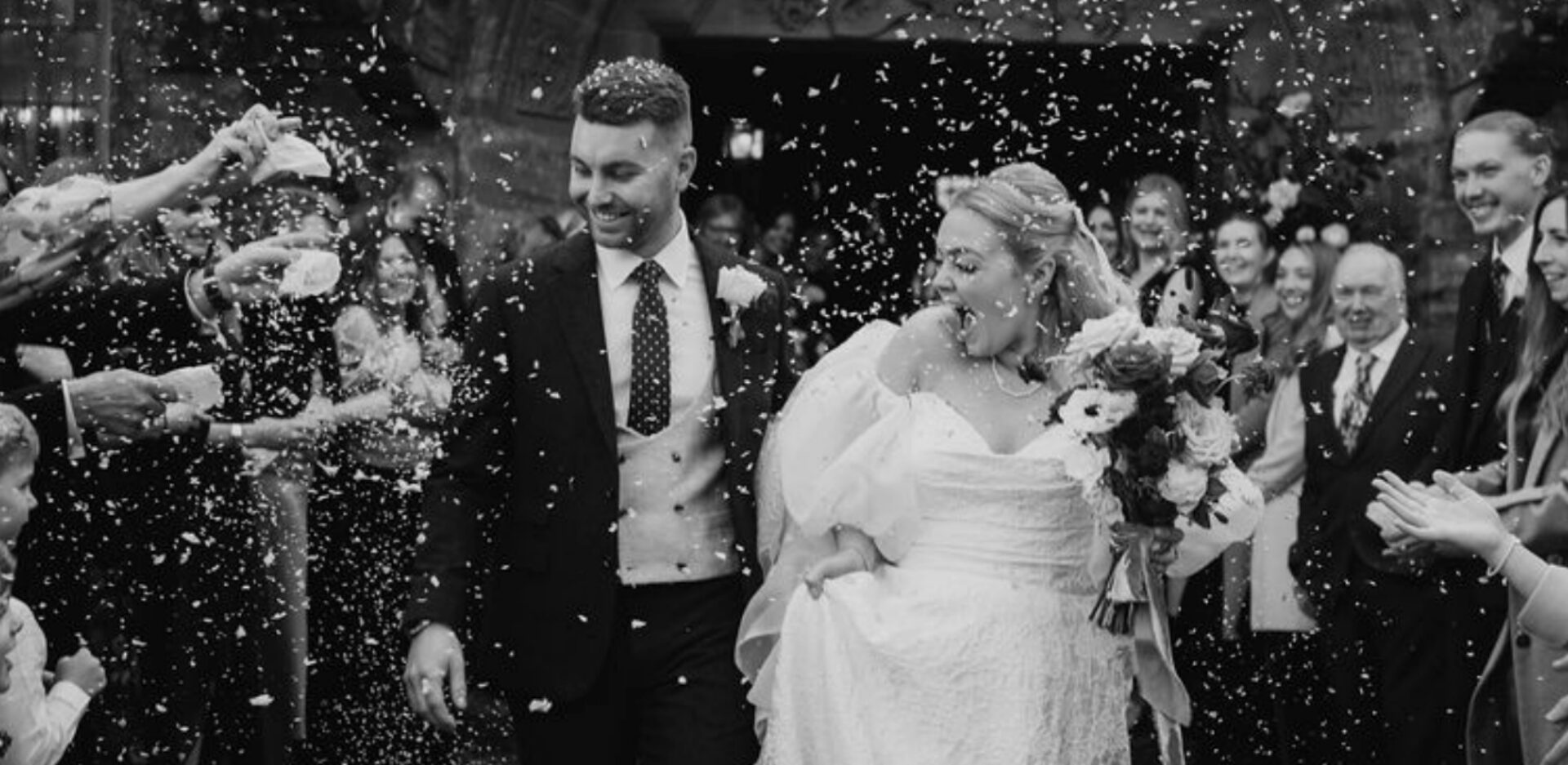 Newly married couple walking through wedding guests throwing confetti after their ceremony.