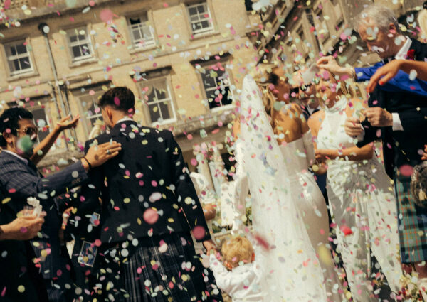 Newlyweds smiling as their wedding guests shower them with confetti following the ceremony.